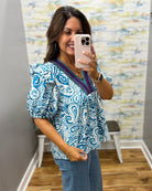 Woman taking a mirror selfie wearing a blue and white patterned top with a colorful trim.