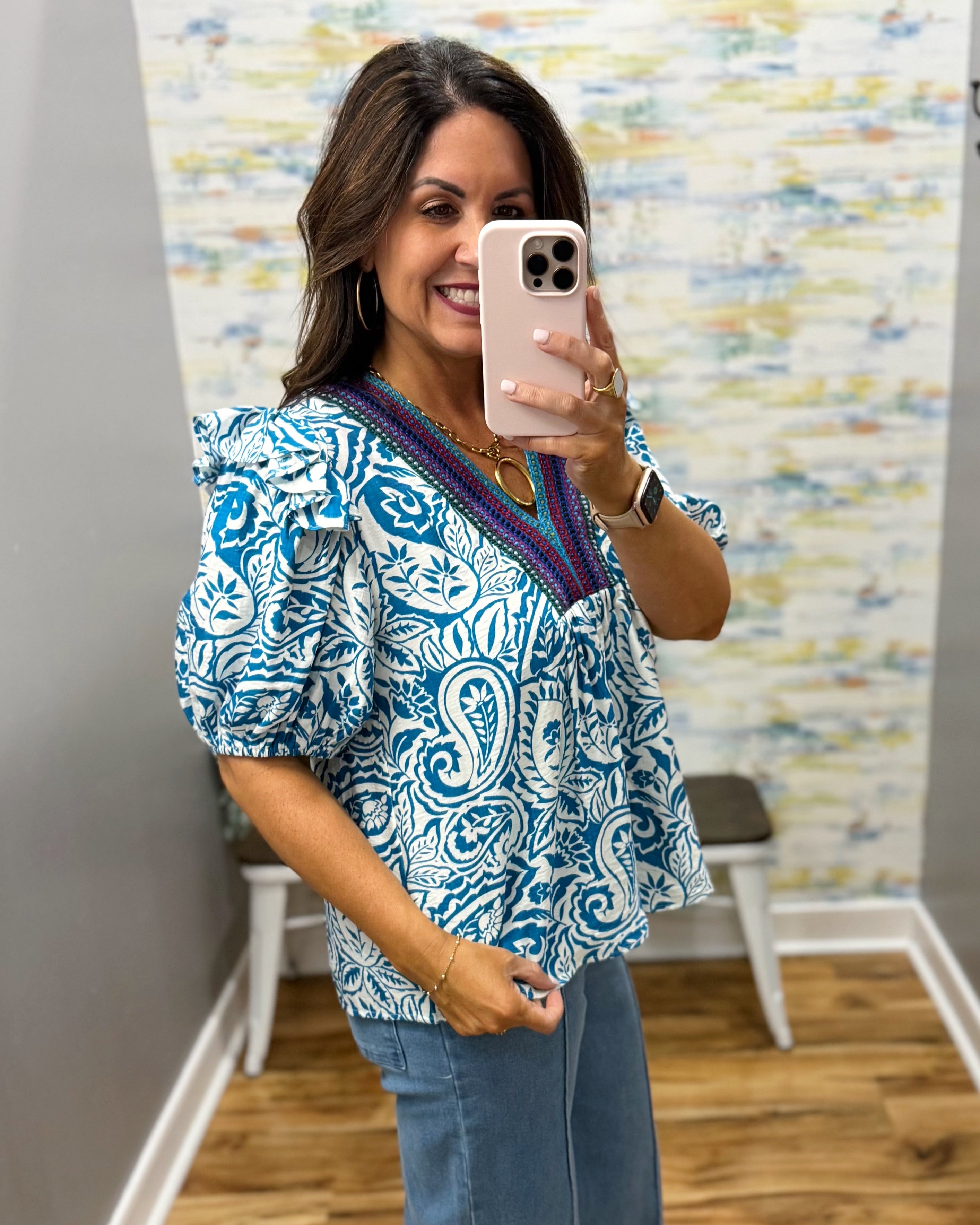 Woman taking a mirror selfie wearing a blue and white patterned top with a colorful trim.