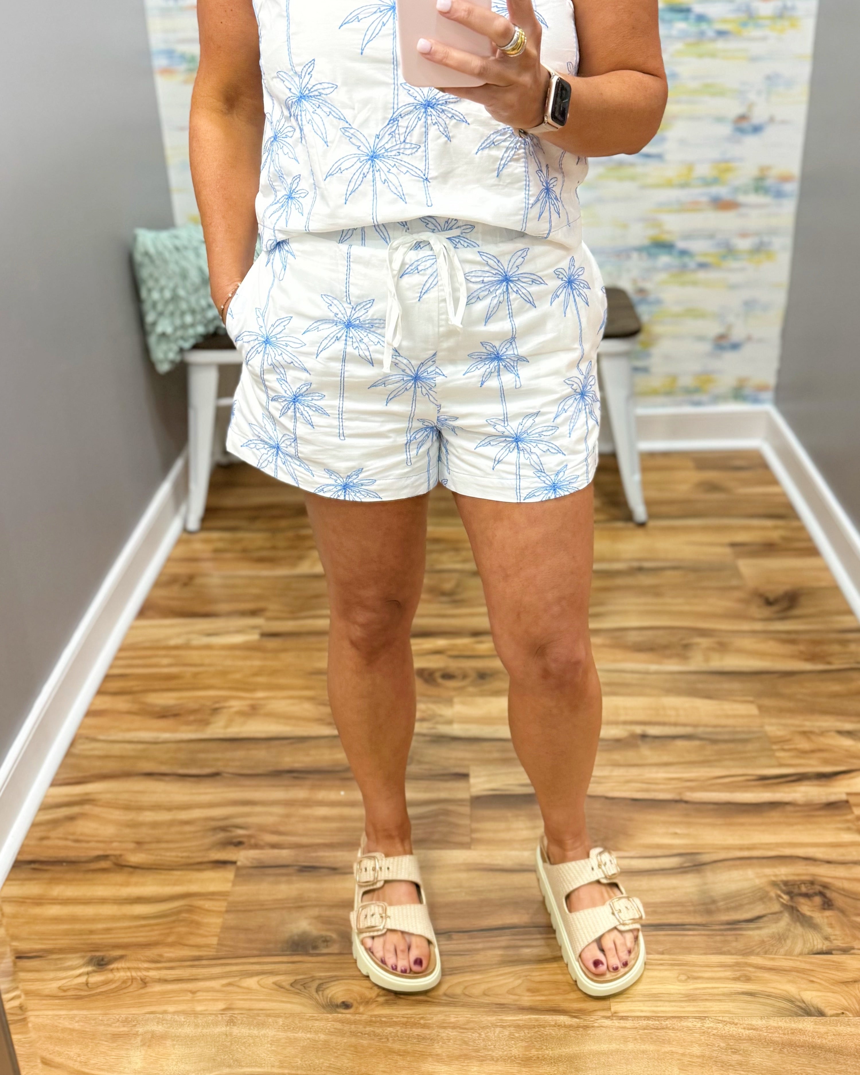 woman wearing white shorts with blue palm trees embroidered on them.