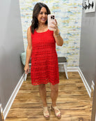 Woman taking a mirror selfie wearing a red crochet dress in a room with a colorful wall.