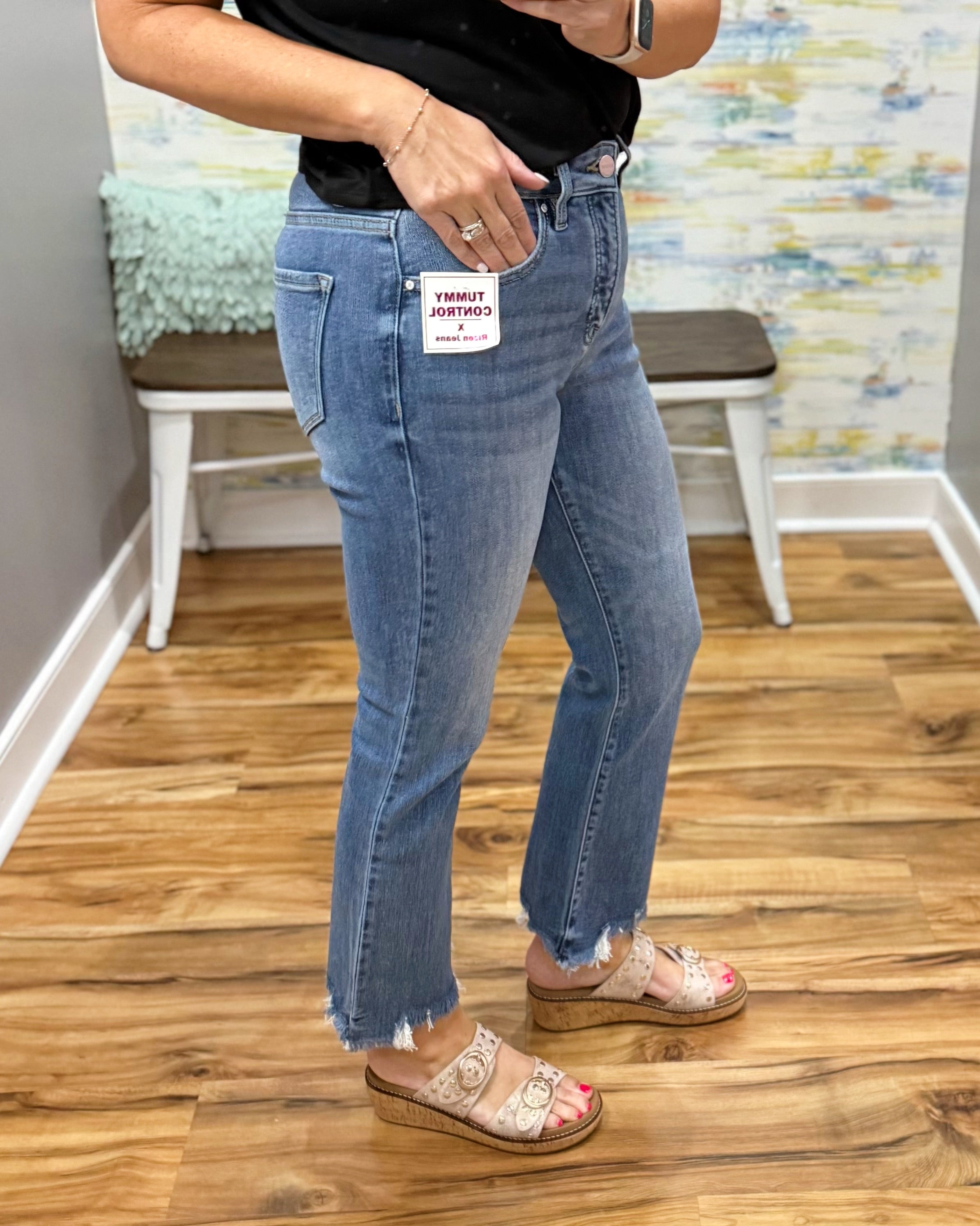 Person wearing blue jeans with a visible brand tag, standing on a wooden floor.