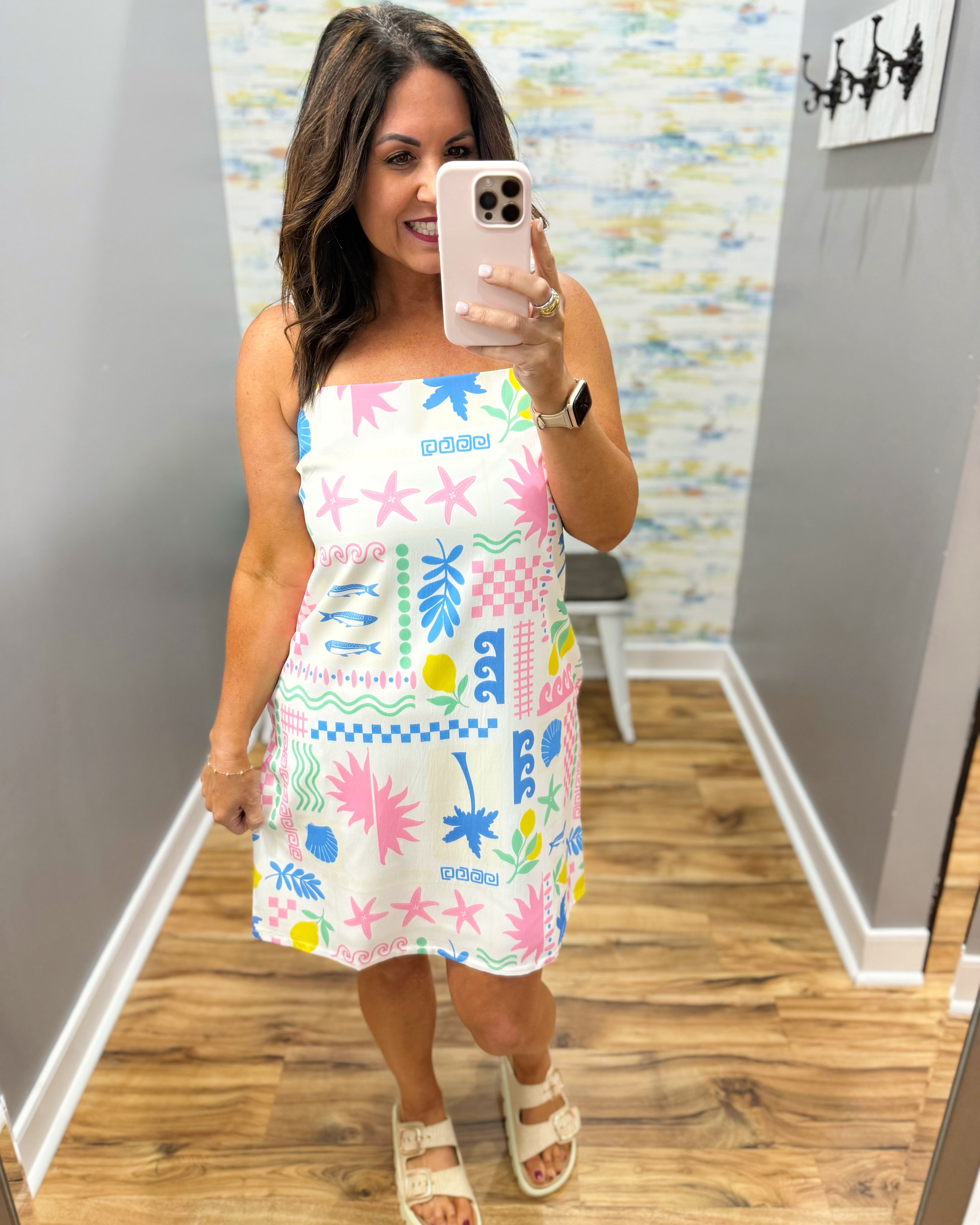Woman wearing a colorful dress with abstract patterns in a room with patterned wallpaper.