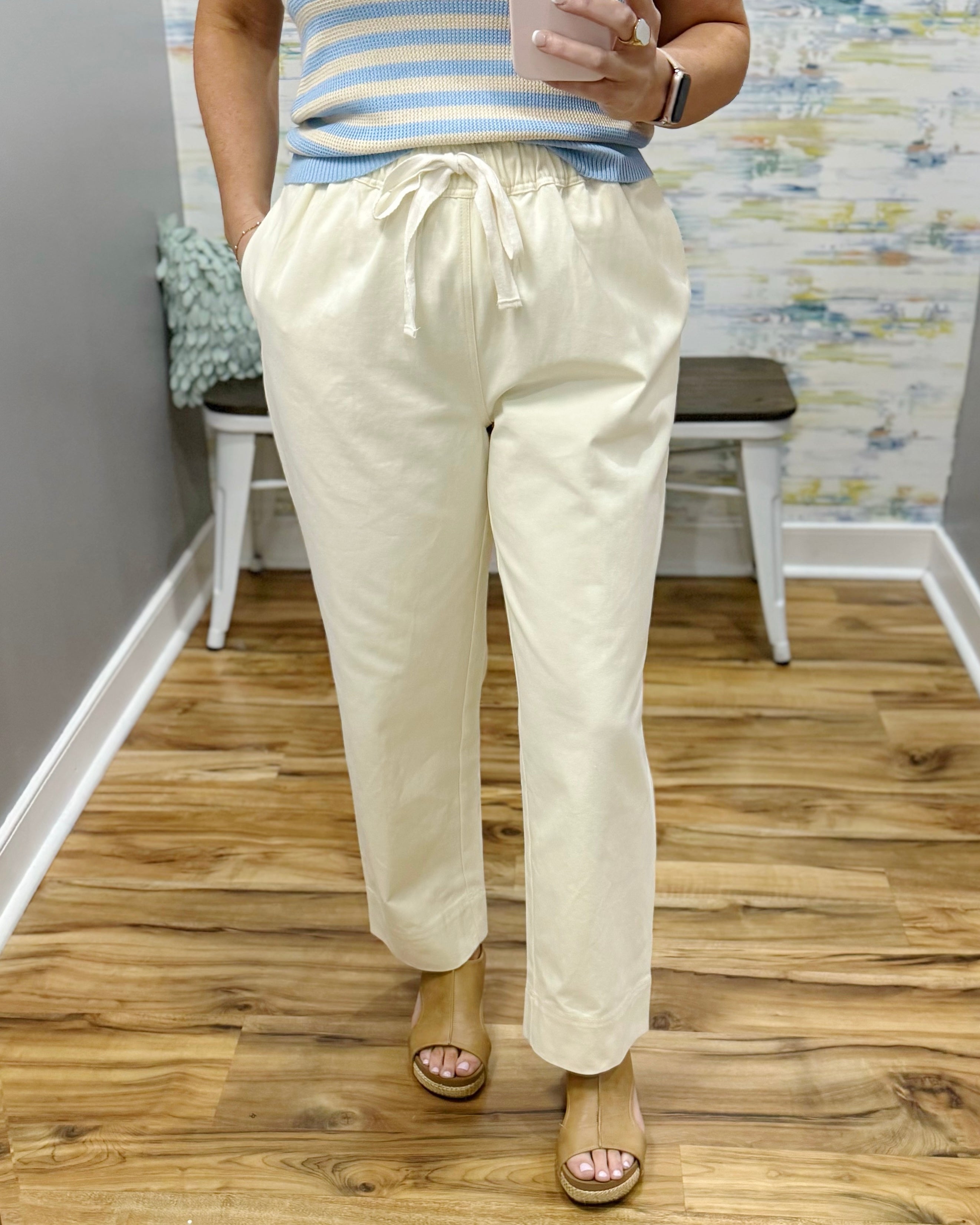 Person wearing light-colored pants and a striped shirt on a wooden floor.