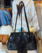 A black crocodile-embossed leather handbag with double shoulder straps, displayed on a mannequin stand in a retail clothing setting.