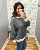 A woman takes a mirror selfie wearing a black and white horizontally striped long-sleeve knit sweater with white ribbed cuffs and hem, paired with blue jeans.