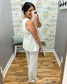 Woman taking a mirror selfie wearing a white sleeveless top and pants in a room with patterned wallpaper.