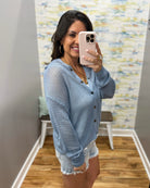 Woman taking a mirror selfie wearing a light blue cardigan and white shorts in a room with a colorful wall.