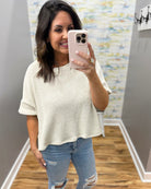 Woman taking a mirror selfie wearing a natural sweater and jeans in a room with a textured wall.