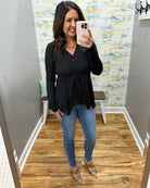 Woman taking a mirror selfie wearing a black top and blue jeans in a room with a patterned wall.