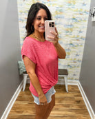 Woman taking a mirror selfie wearing a pink shirt and denim shorts in a room with a colorful wall.
