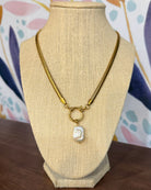 Chansuttpearls Delilah gold chain necklace with a toggle clasp and a small white carved pendant, displayed on a beige woven jewelry bust against a colorful patterned backdrop.