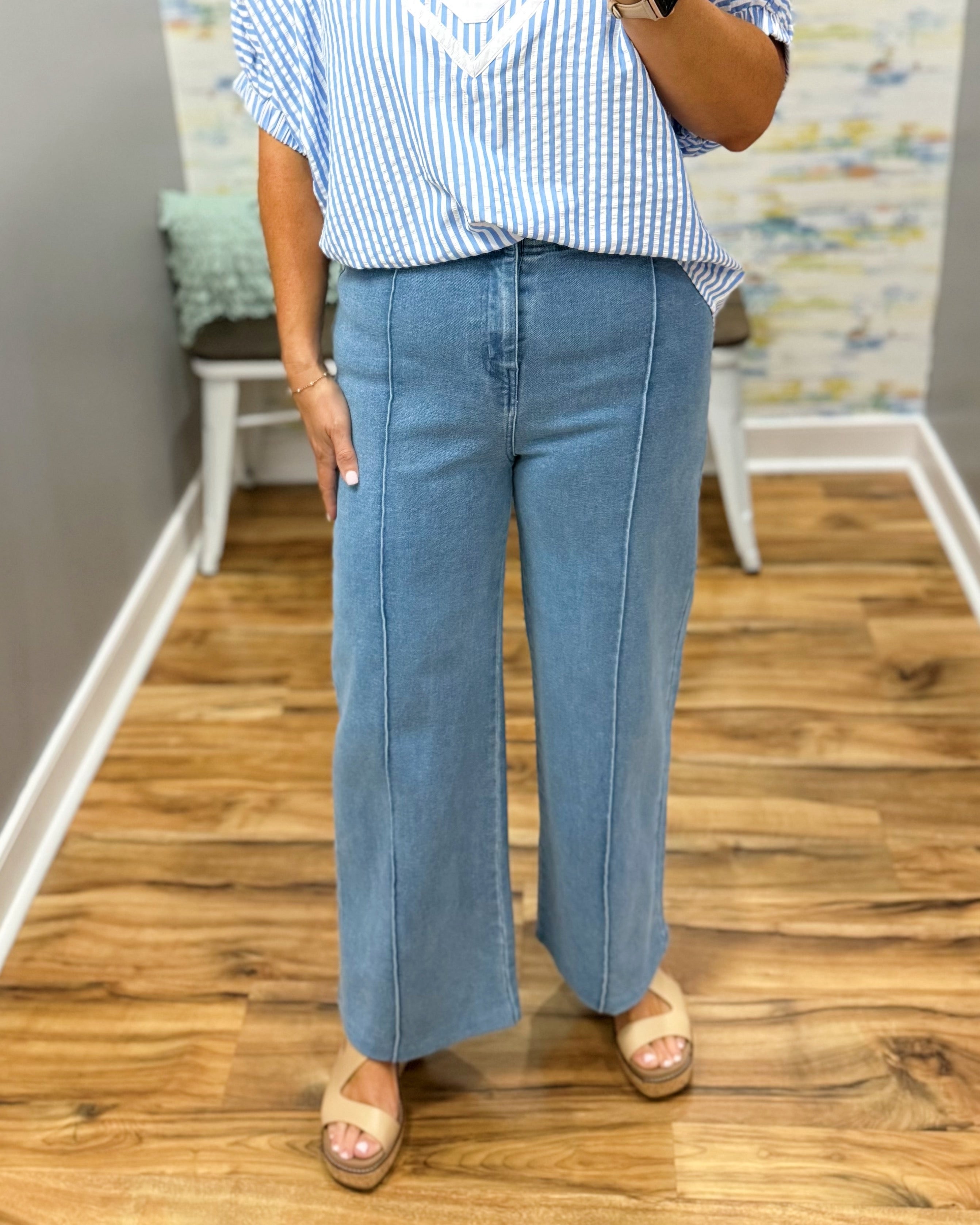 Person wearing a blue and white striped shirt and light blue jeans on a wooden floor.