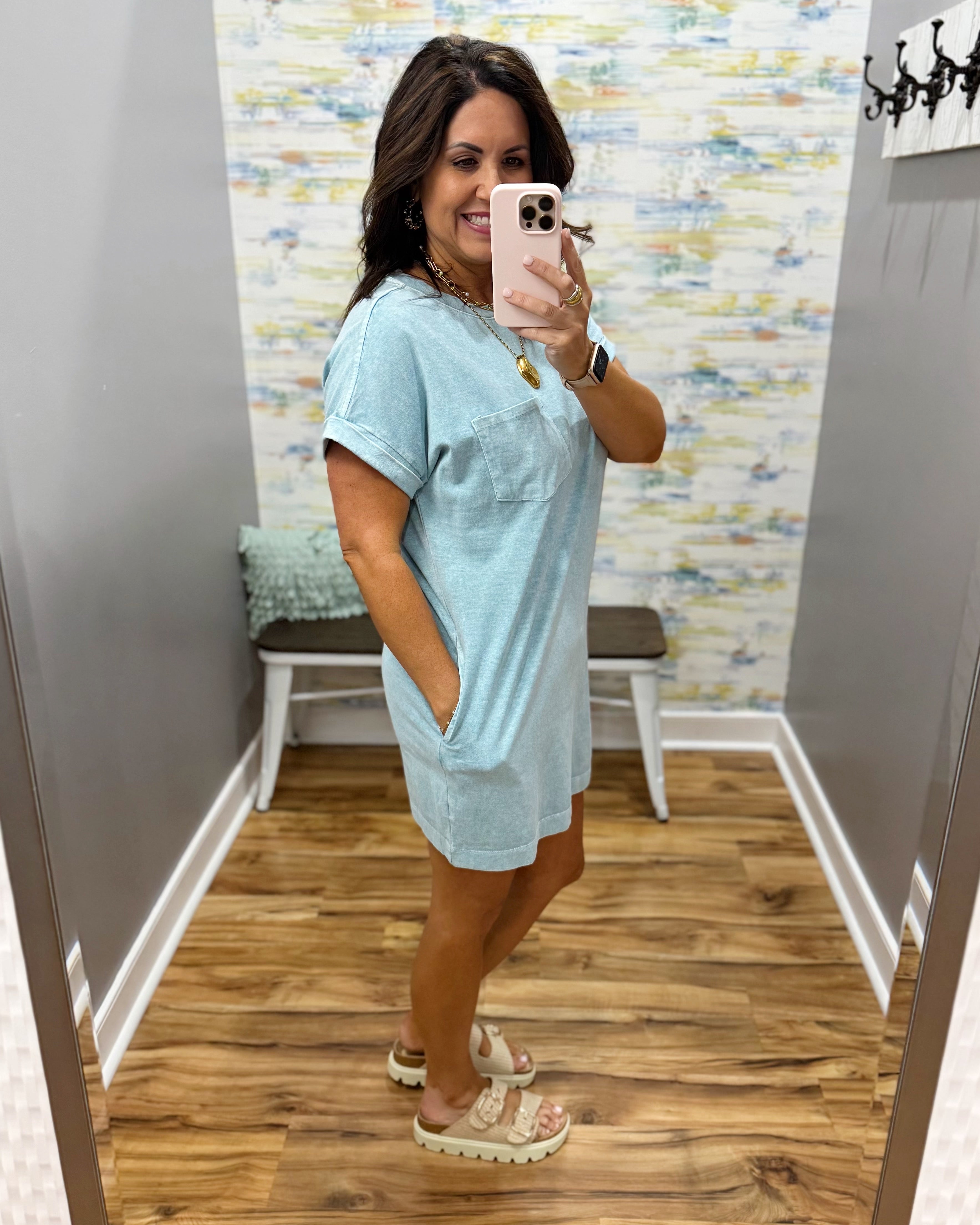 Woman taking a mirror selfie wearing a light blue dress in a room with a colorful wall.