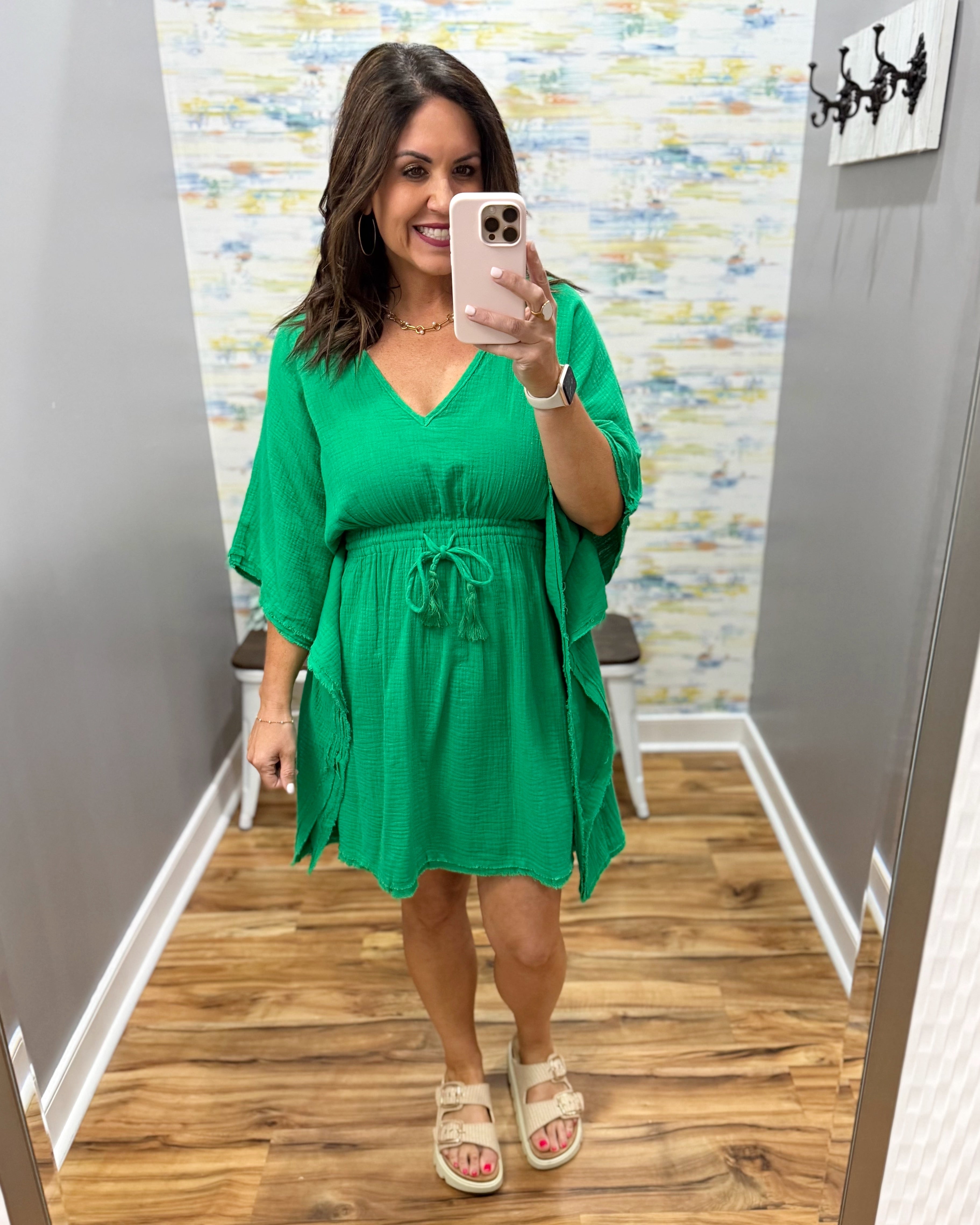 Woman in a green dress taking a mirror selfie in a room with a colorful wall.