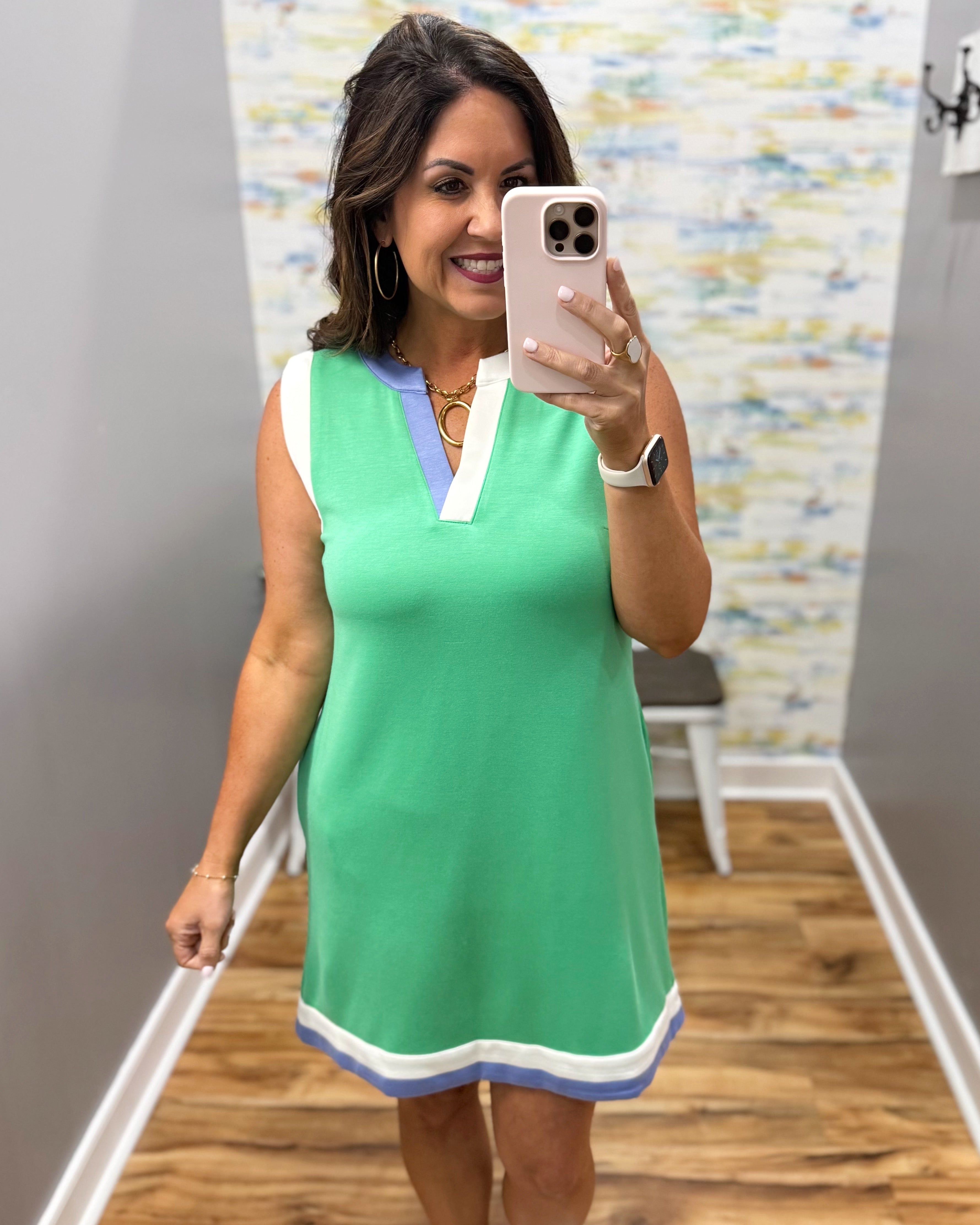 Woman taking a mirror selfie wearing a green dress with a colorful wall in the background