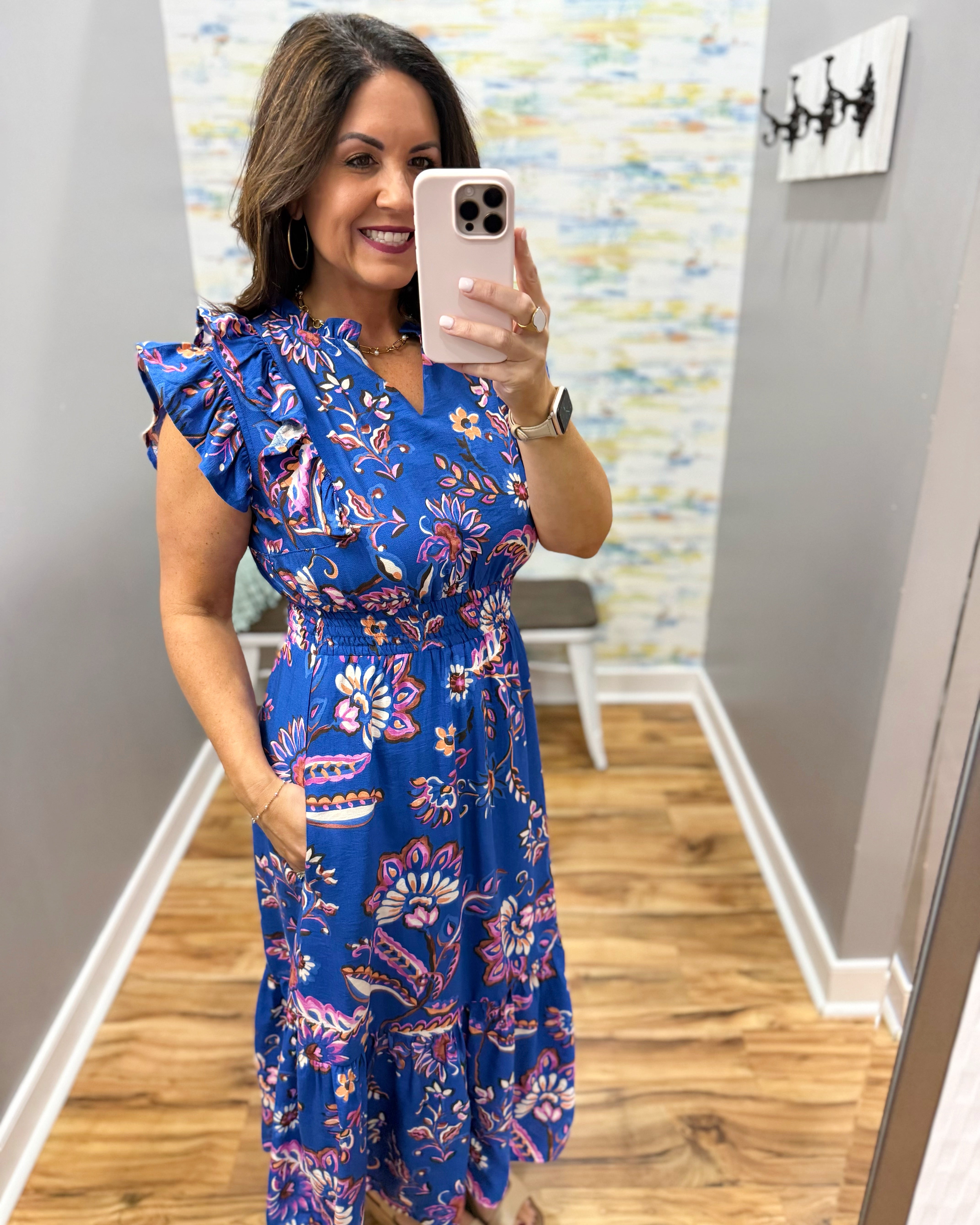 Woman taking a mirror selfie wearing a blue floral dress.