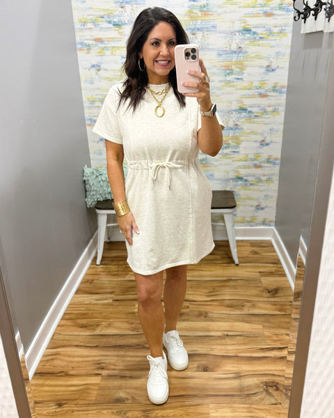 Woman wearing a neutral dress and white sneakers.