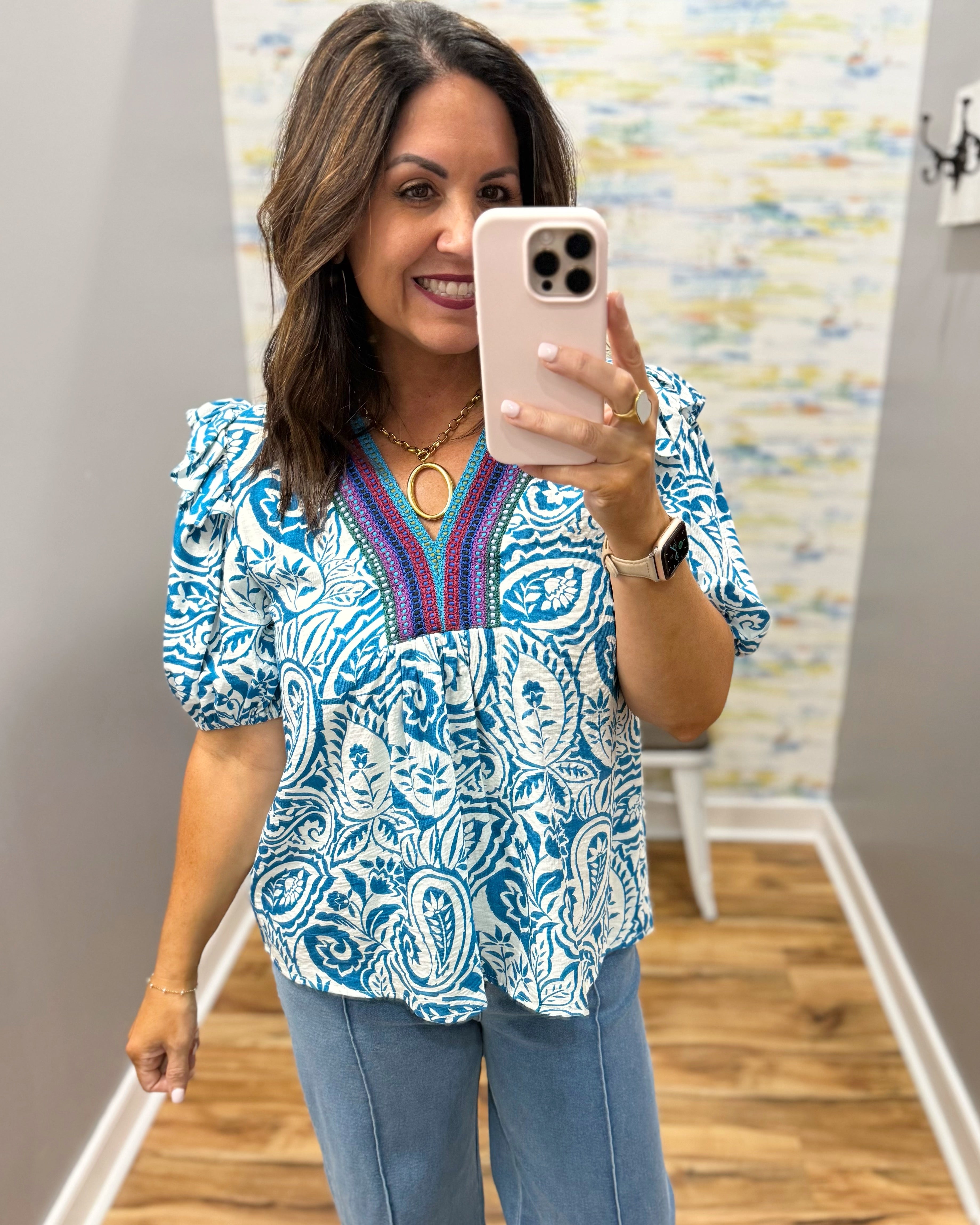 Woman taking a mirror selfie wearing a blue patterned blouse and jeans.