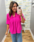 Woman taking a mirror selfie wearing a bright pink top and blue jeans in a room with colorful wall art.