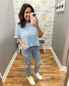 Woman taking a mirror selfie wearing a light blue sweater and ripped jeans in a room with a patterned wall.