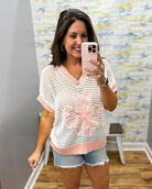 woman wearing a cream sweater with pink floral print.