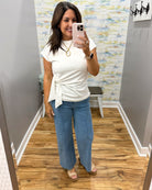 Woman taking a mirror selfie wearing a white top and blue jeans in a room with patterned wallpaper.