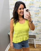 Woman taking a mirror selfie wearing a yellow top and denim shorts in a room with a patterned wall.