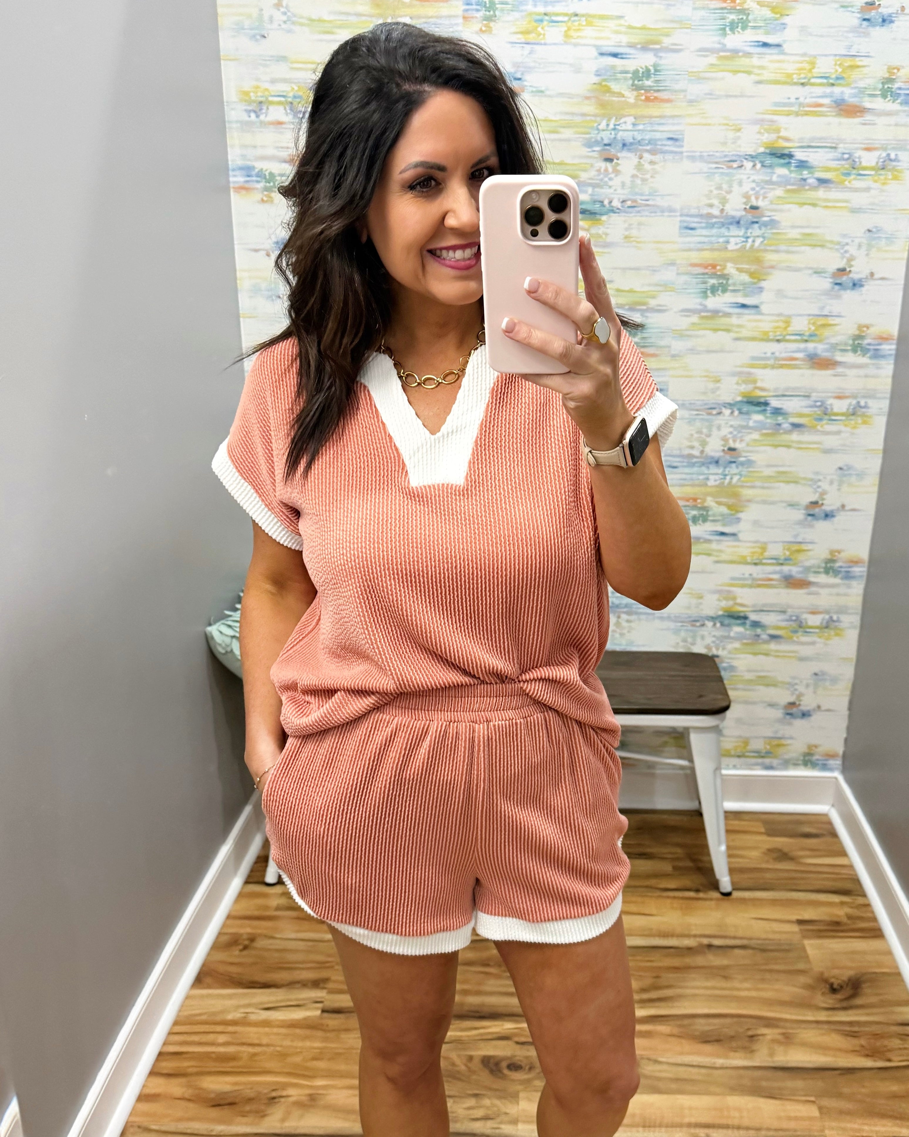 Woman taking a mirror selfie wearing a pink ribbed lounge set in a room with a colorful wall.