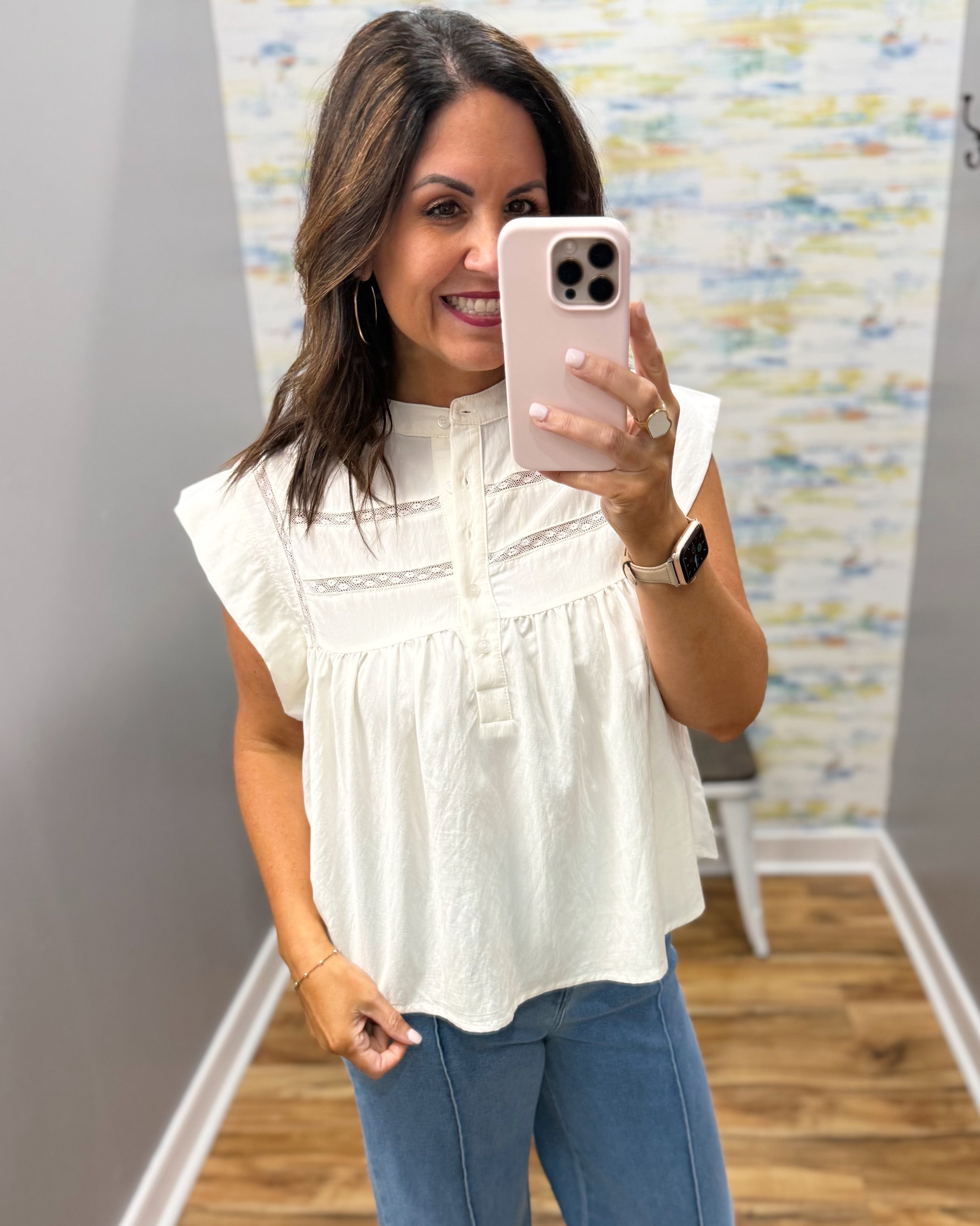 Woman taking a mirror selfie wearing a white blouse and blue jeans in a room with a colorful wall.