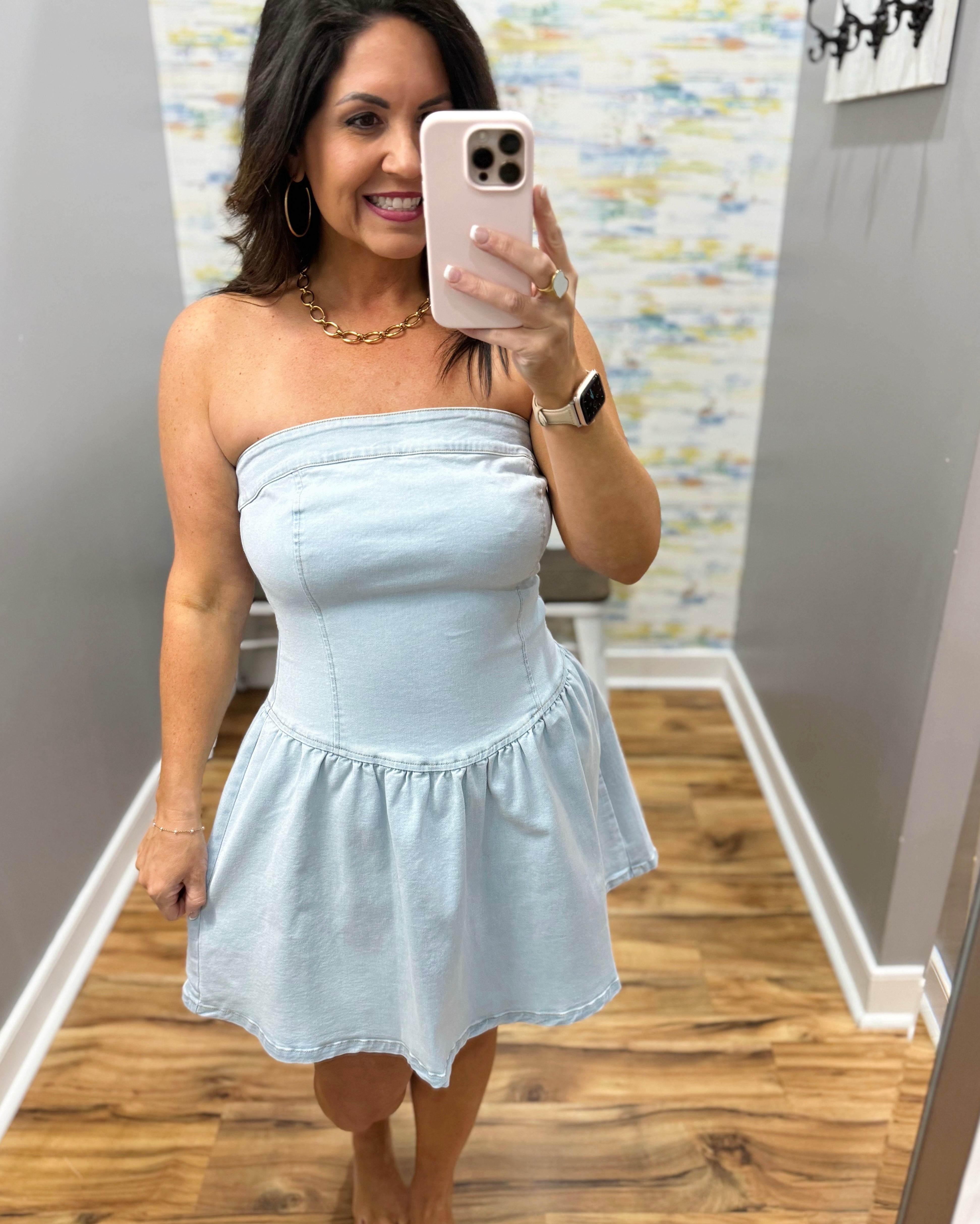 Woman taking a mirror selfie wearing a light blue strapless dress in a room with a colorful wall.