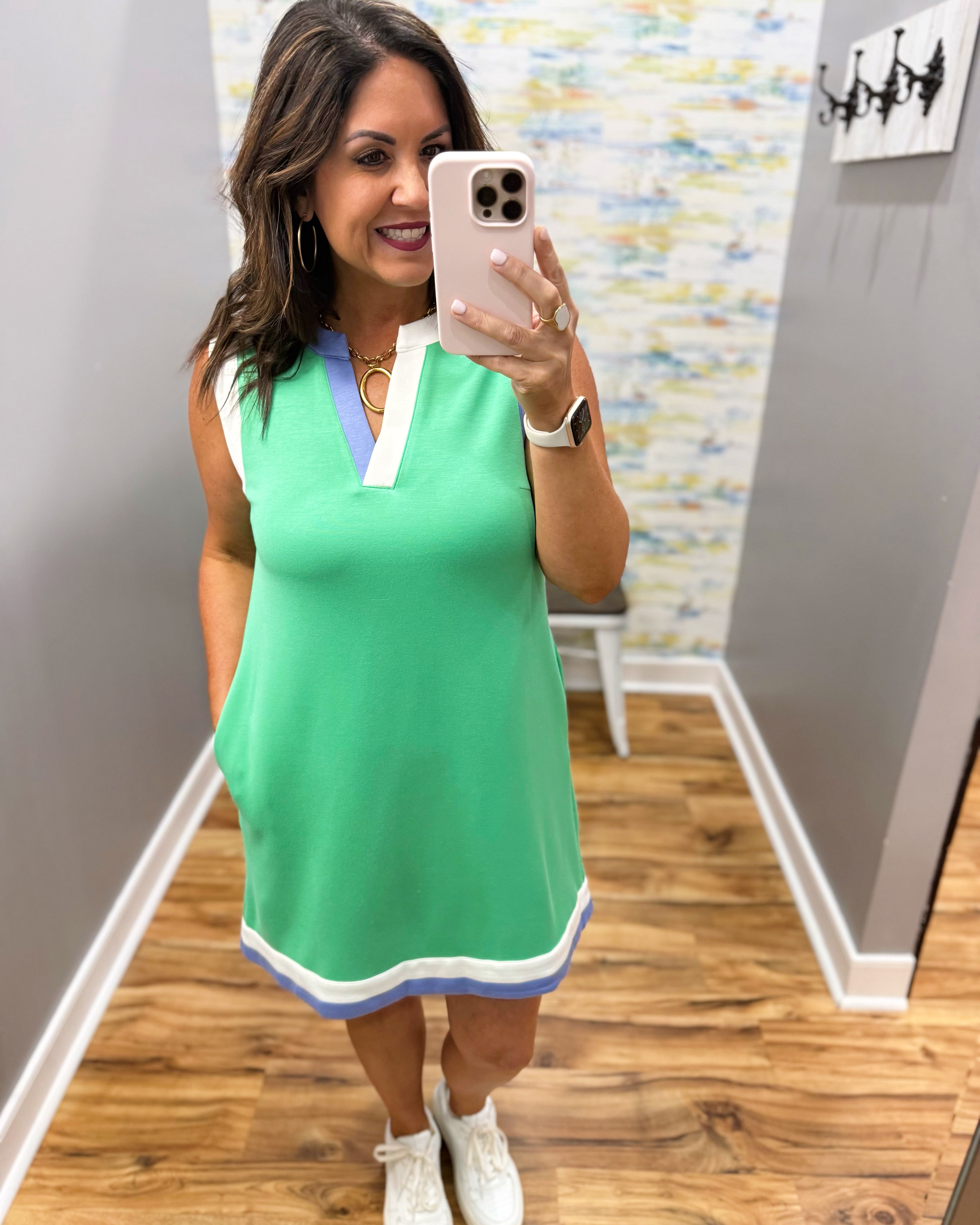 Woman taking a mirror selfie wearing a green dress with white accents.