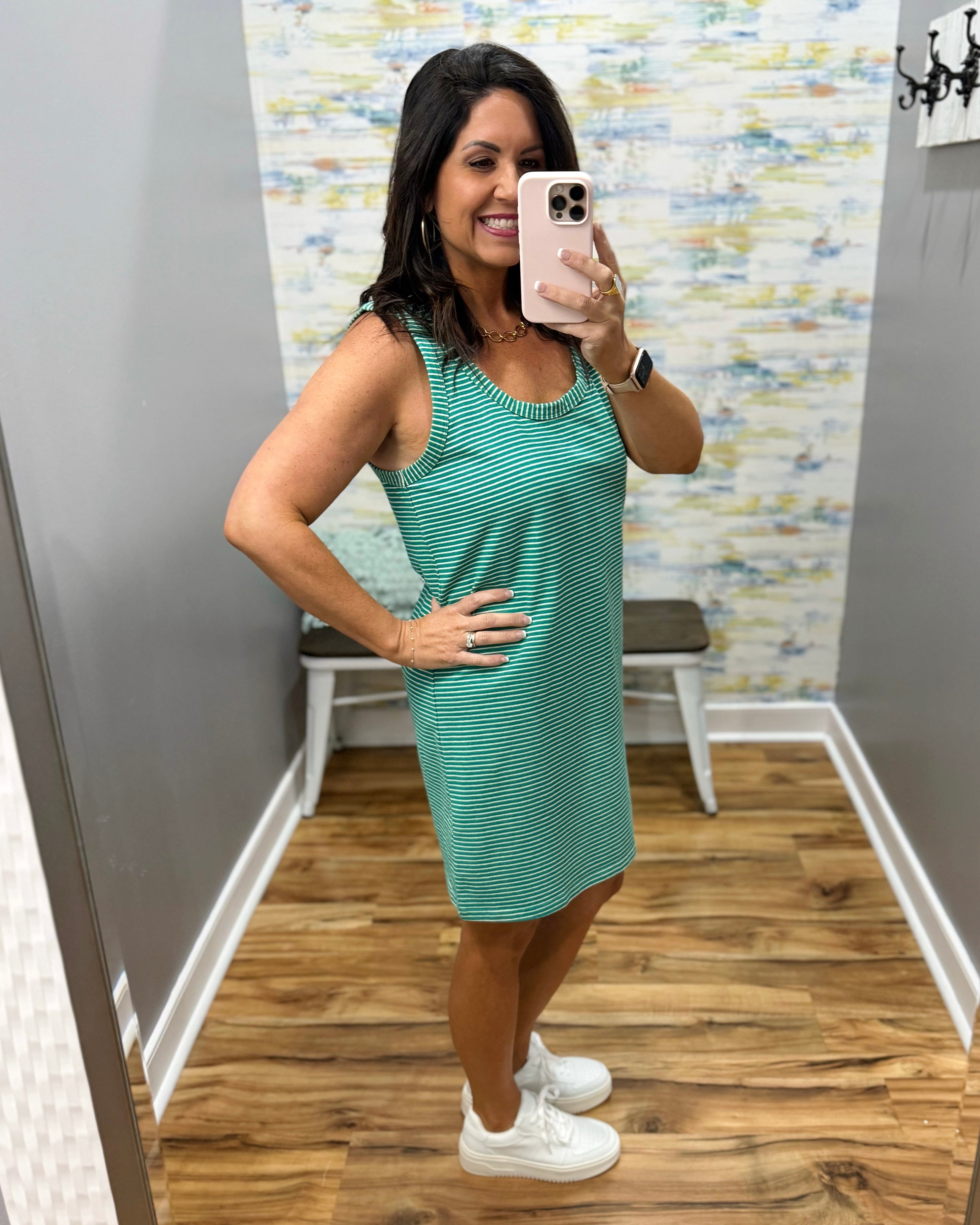 Woman taking a mirror selfie wearing a green dress in a room with a patterned wall.