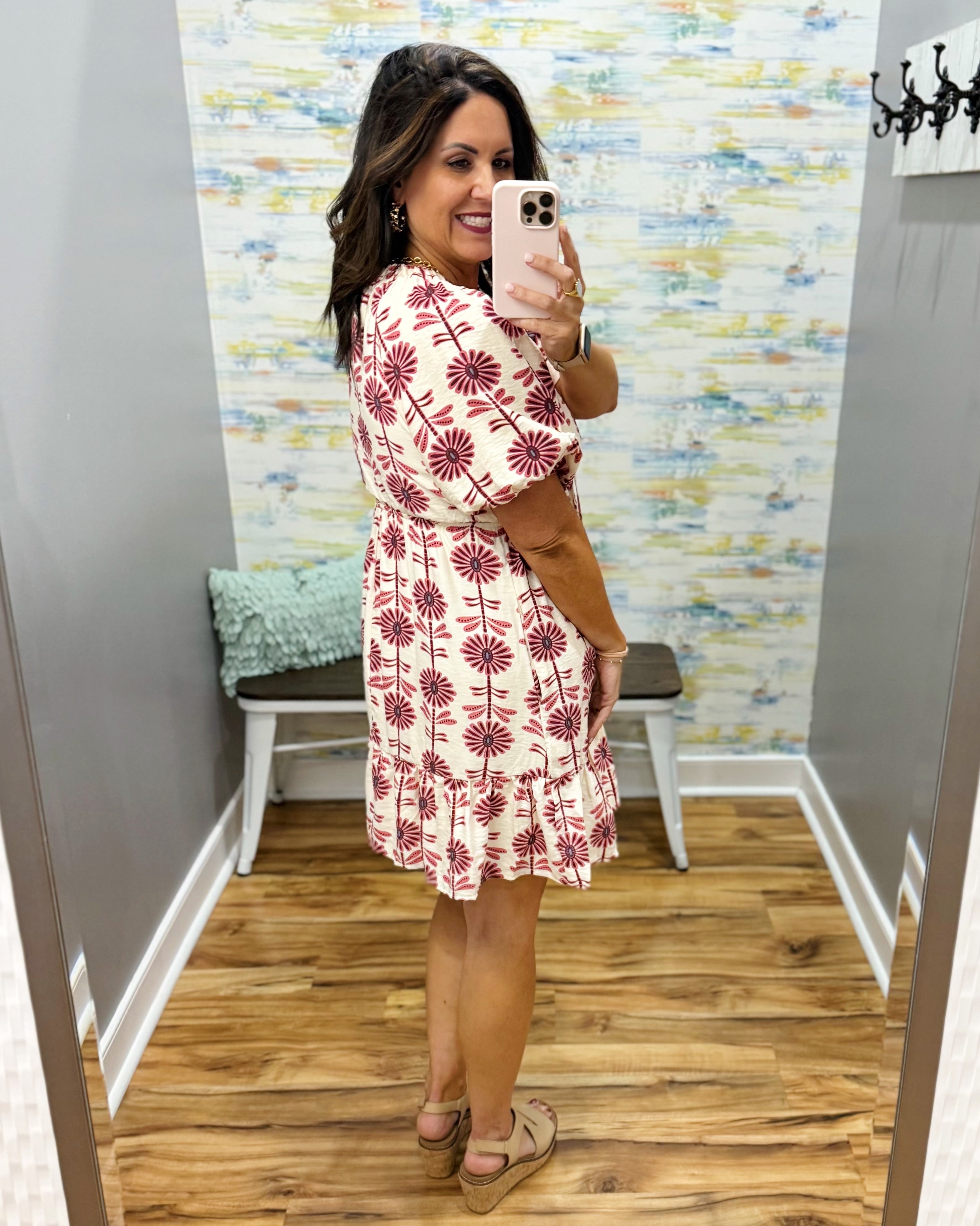 Woman taking a mirror selfie wearing a red floral dress in a store.