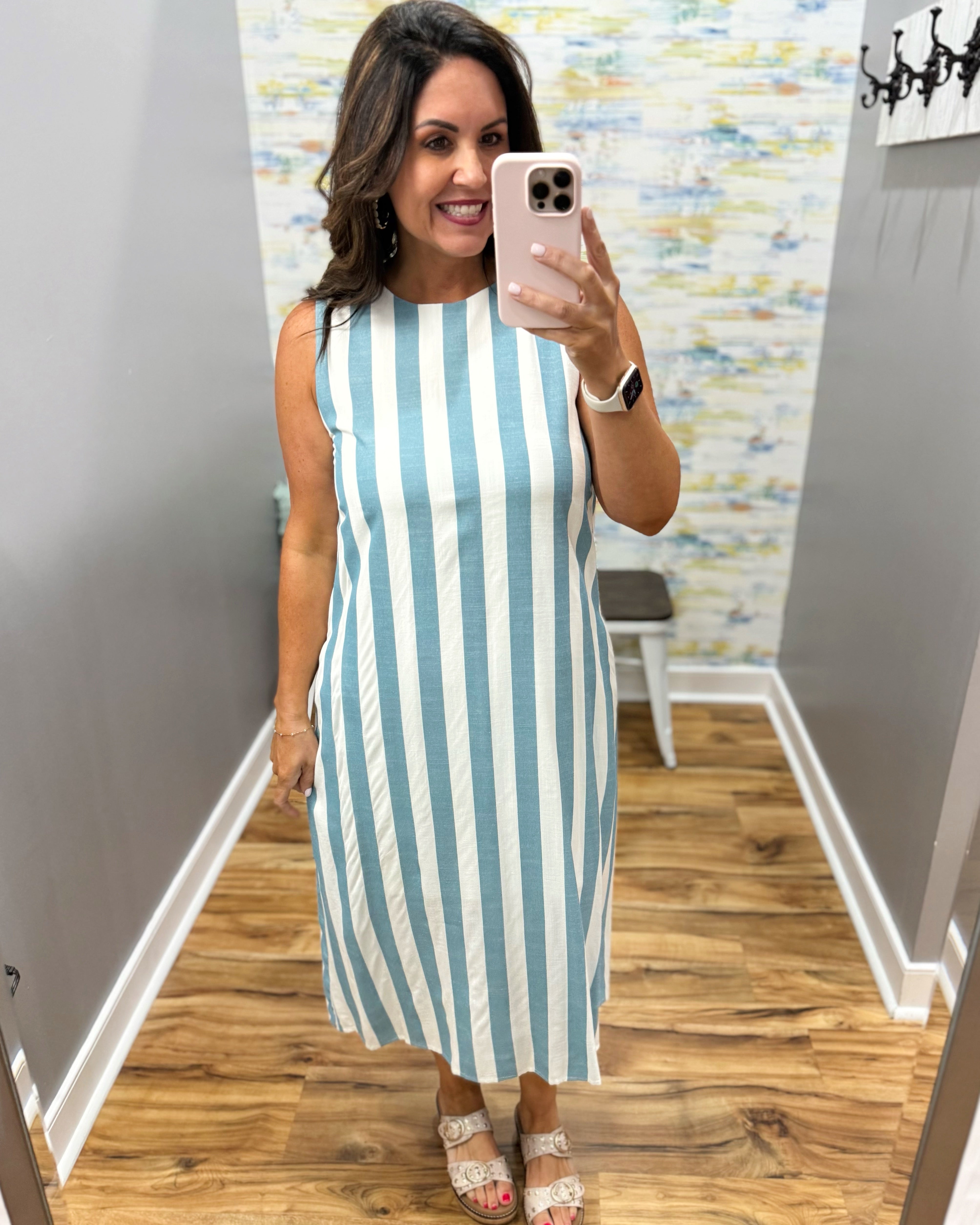 Woman taking a mirror selfie wearing a blue and white striped dress in a room with wooden flooring and a colorful wall.
