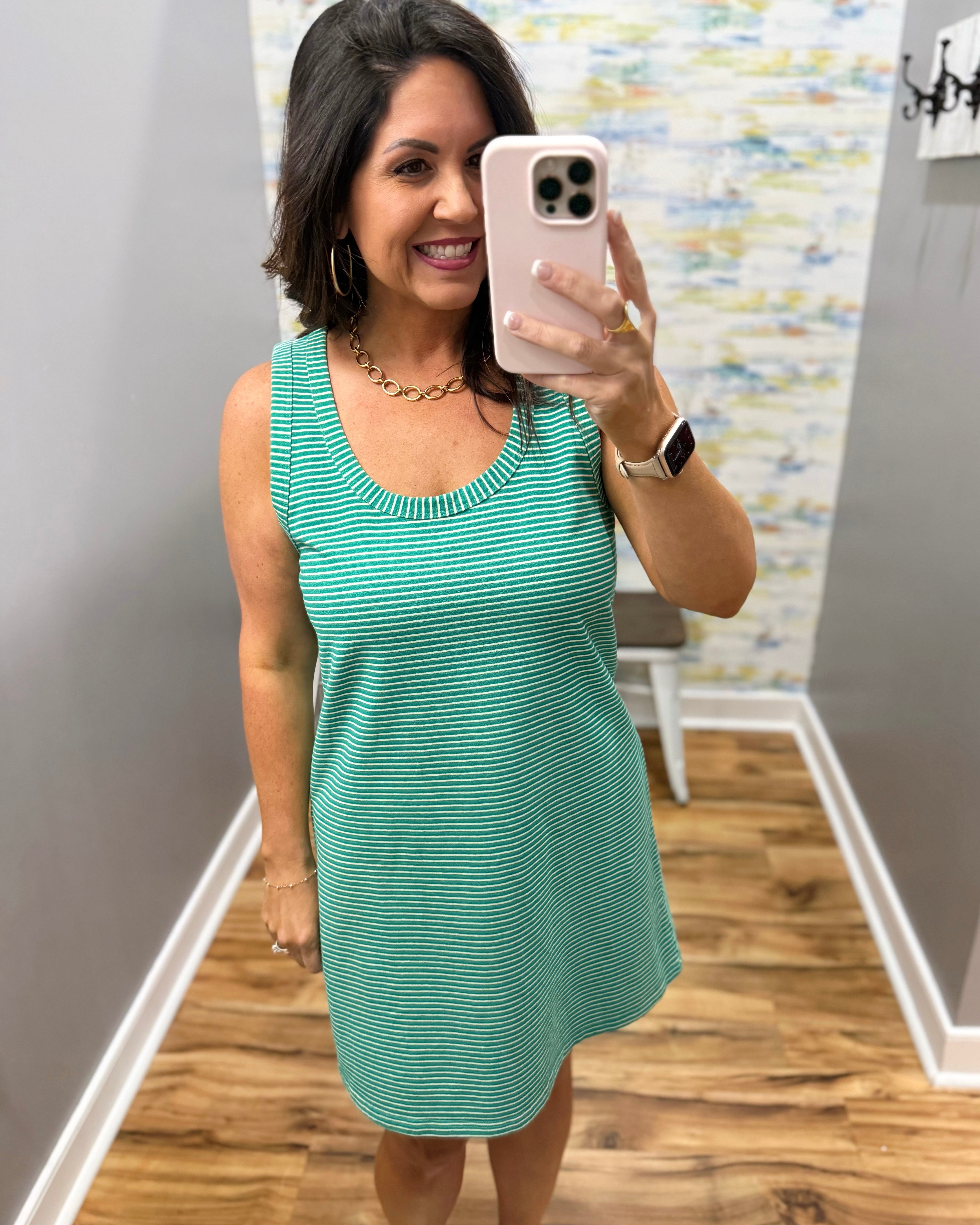 Woman taking a mirror selfie wearing a green dress in a room with a patterned wall.