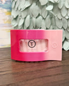 Pink container with a brand logo on a wooden surface with a leafy background