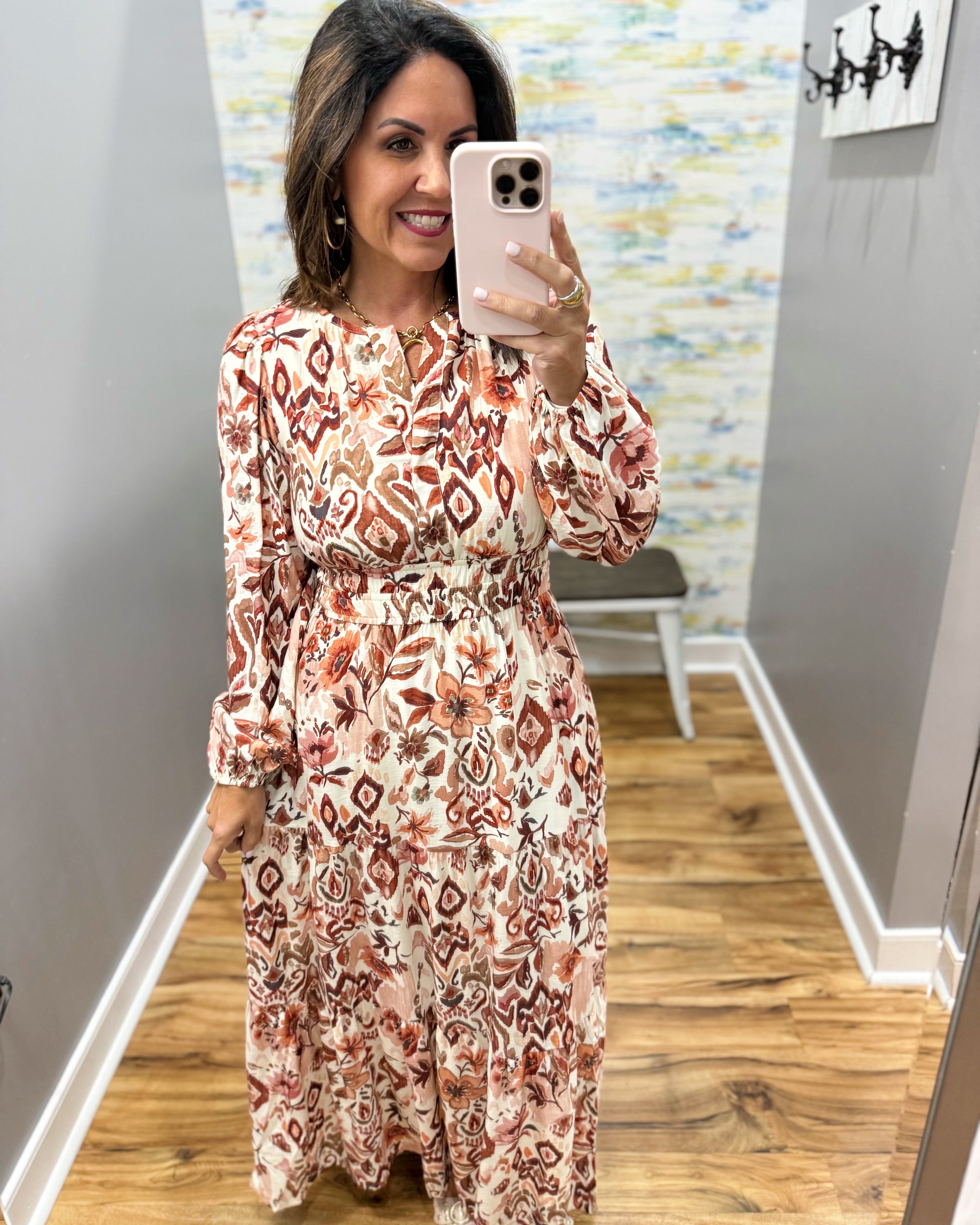 A woman takes a mirror selfie in a boutique showing a long-sleeve midi dress with a rust and beige geometric pattern on a cream background.