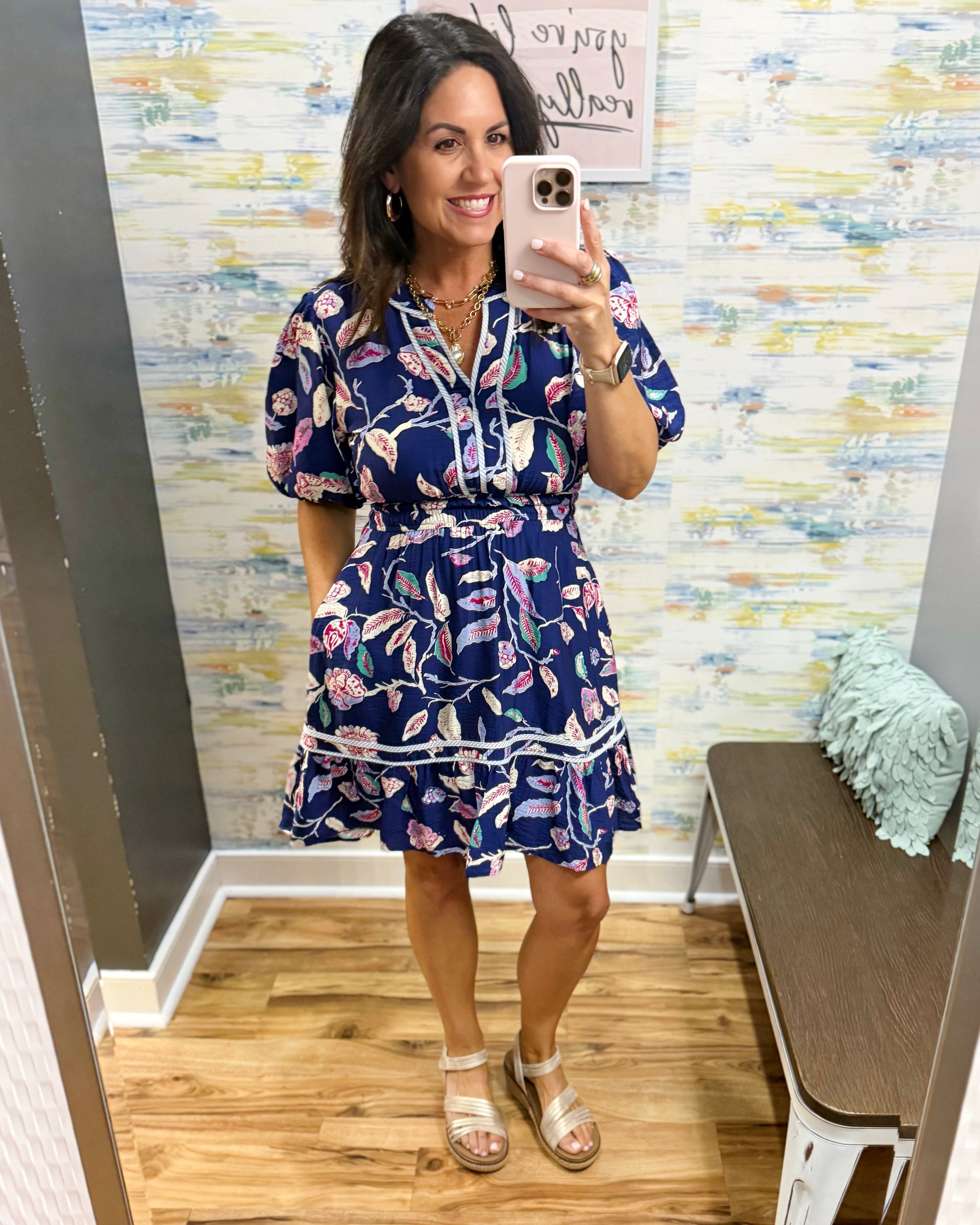 Woman taking a mirror selfie wearing a floral dress in a store.