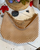 A brown and beige checkered shoulder bag with a gold chain strap, displayed on a white wooden surface with autumn-themed props.