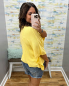 woman wearing a yellow dolman sleeve top with denim shorts.