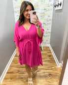 Woman taking a mirror selfie wearing a bright pink dress in a room with a colorful wall.