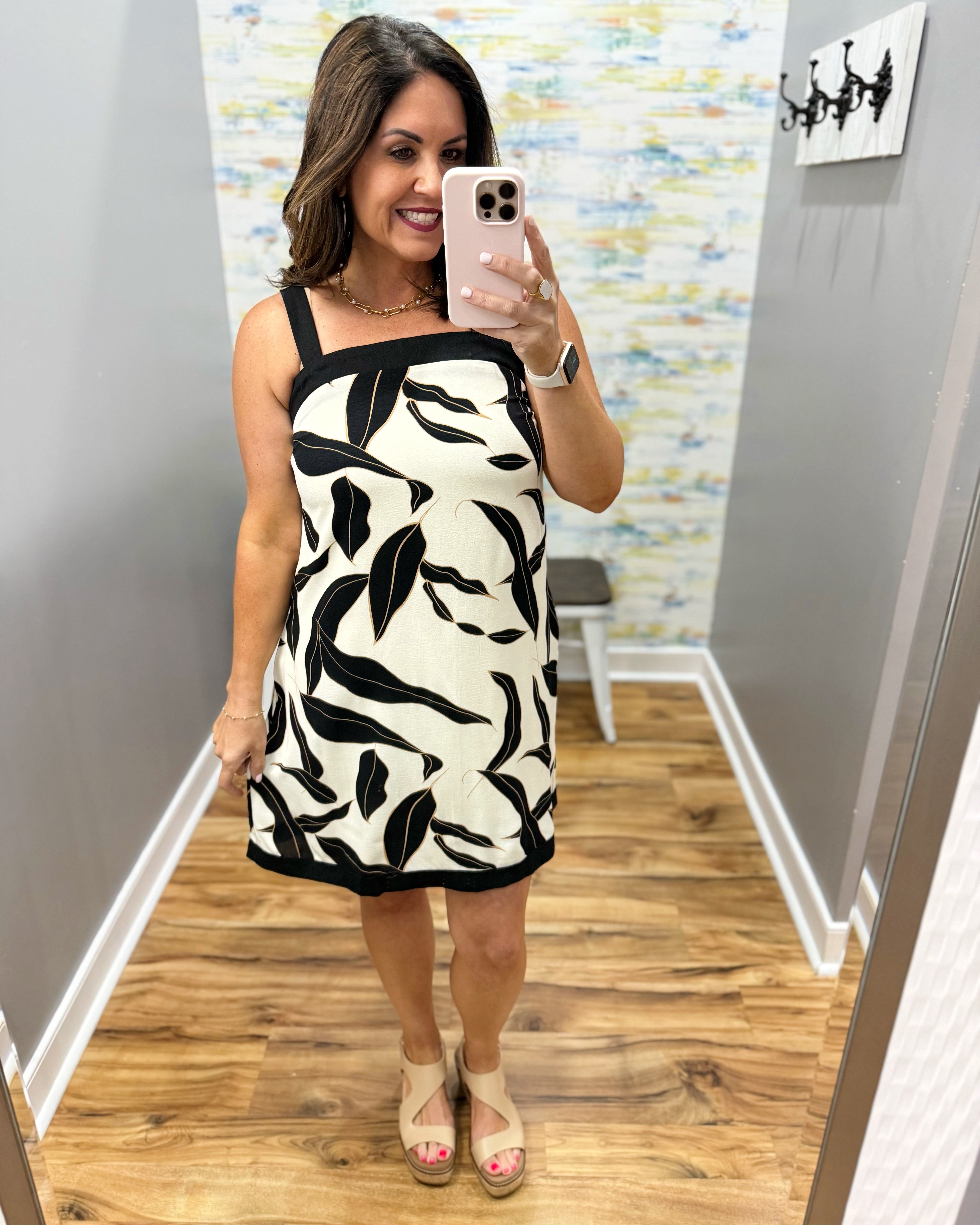 Woman taking a mirror selfie wearing a black and white patterned dress in a room with a colorful wall.