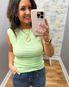Woman wearing a light green top and blue jeans, holding a pink phone.