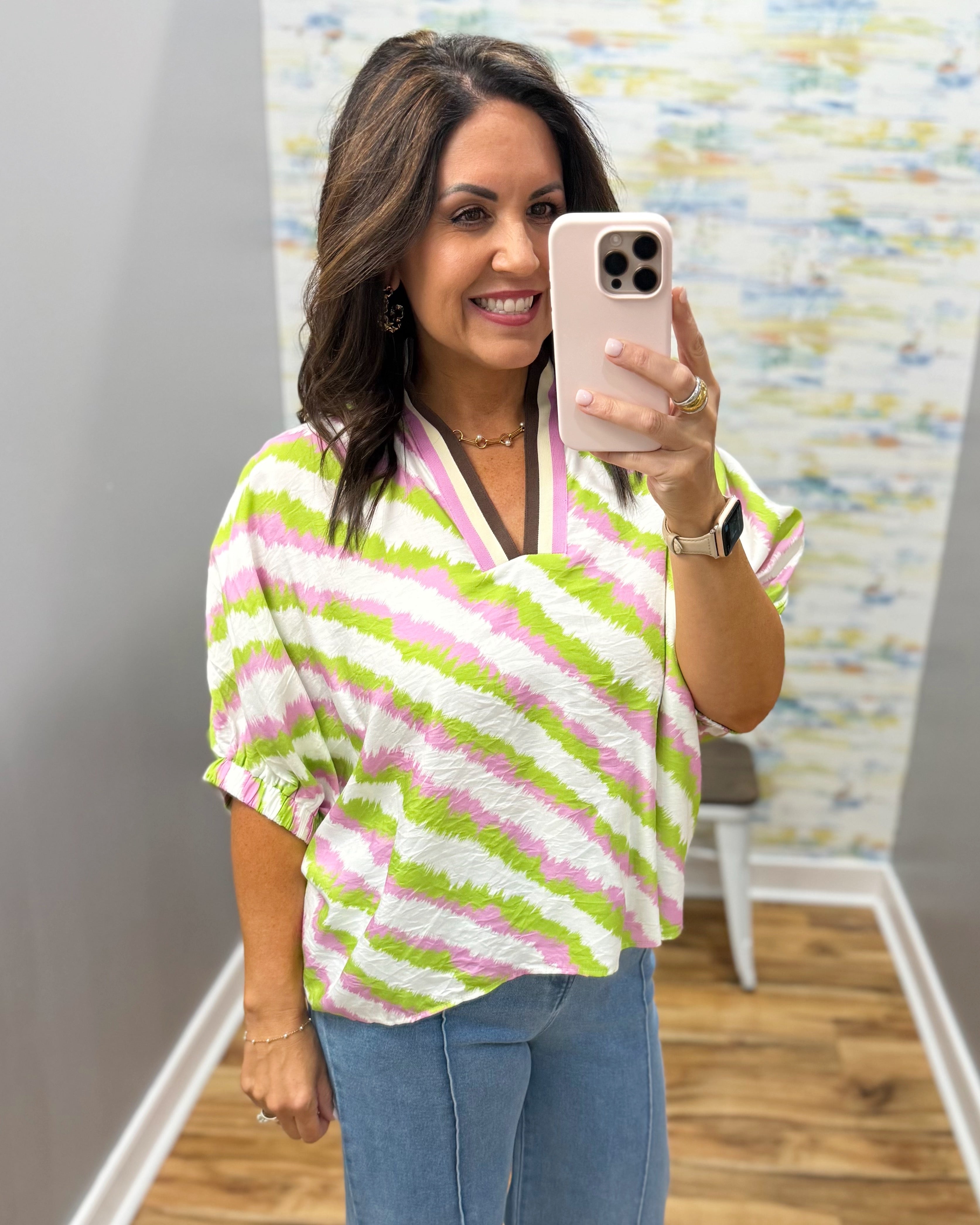 Woman taking a mirror selfie wearing a colorful striped shirt in a room with a patterned wall.