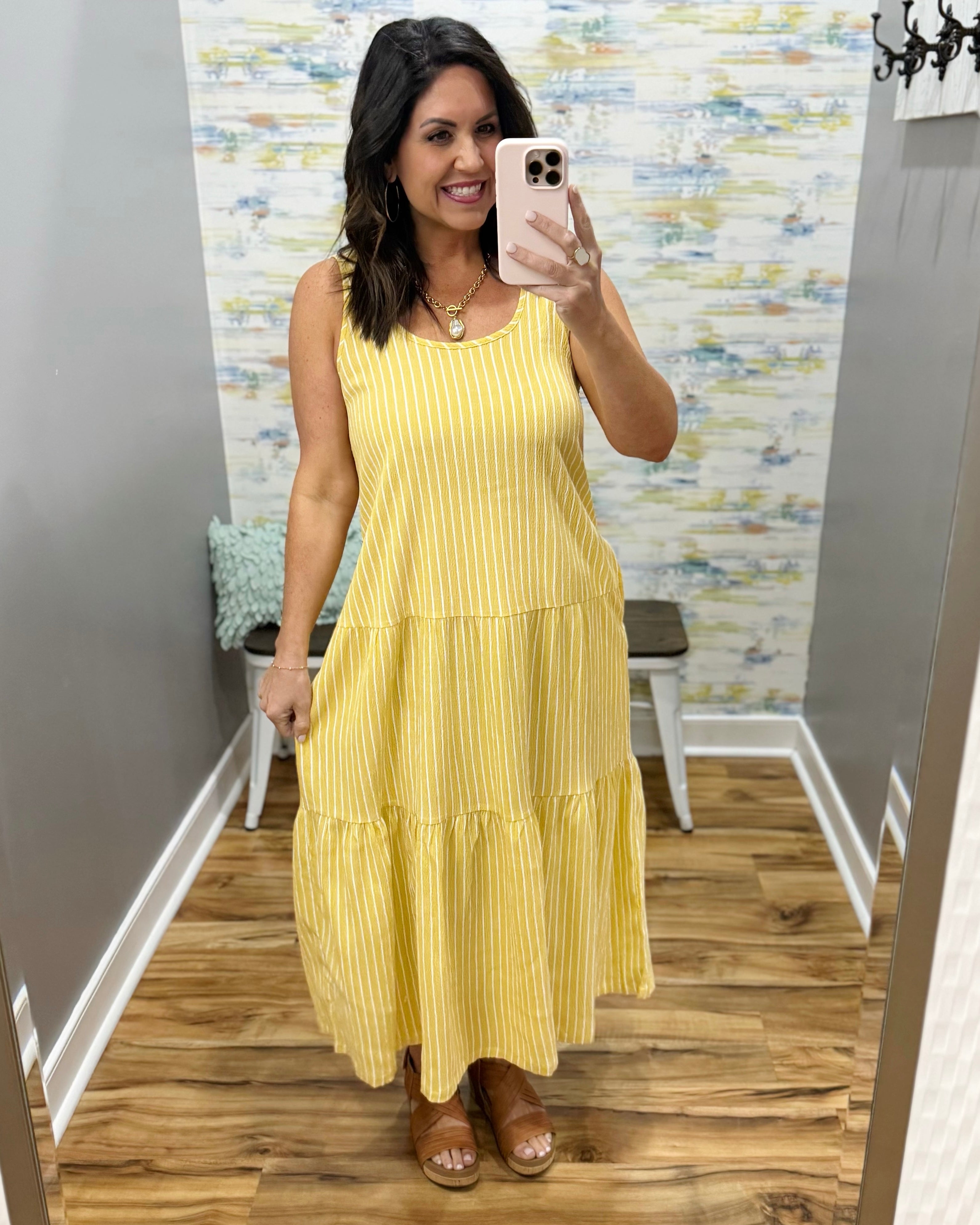 Woman taking a mirror selfie wearing a yellow dress in a room with patterned wallpaper.
