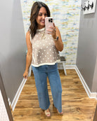 Woman taking a mirror selfie wearing a polka dot top and blue jeans in a room with a colorful wall.