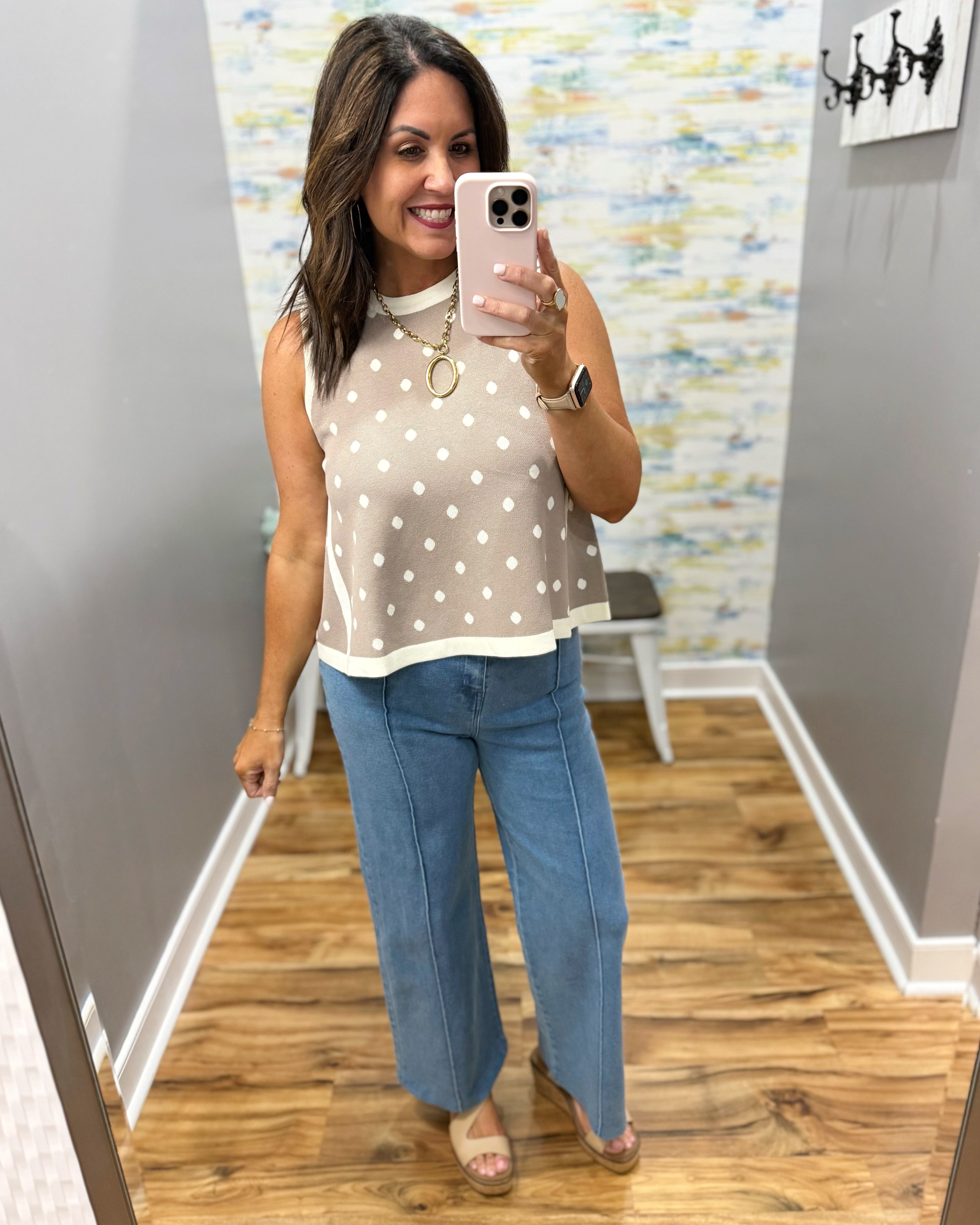 Woman taking a mirror selfie wearing a polka dot top and blue jeans in a room with a colorful wall.