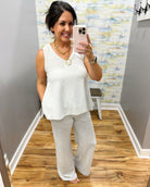 Woman taking a mirror selfie wearing a white sleeveless top and light gray pants in a room with a colorful wall.