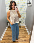 Woman taking a mirror selfie wearing a polka dot top and jeans in a room with a textured wall.