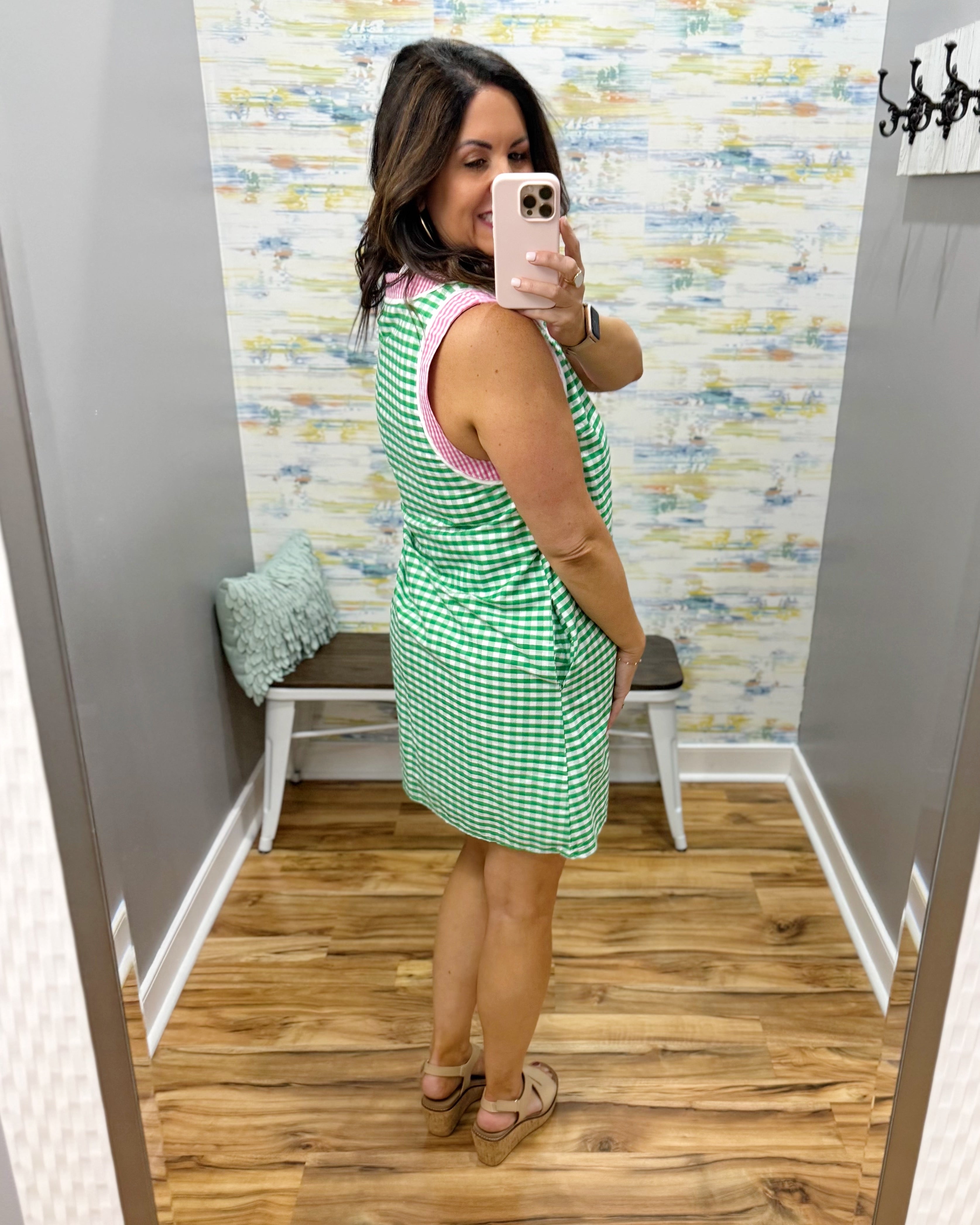 Woman taking a mirror selfie wearing a green checkered dress in a fitting room.